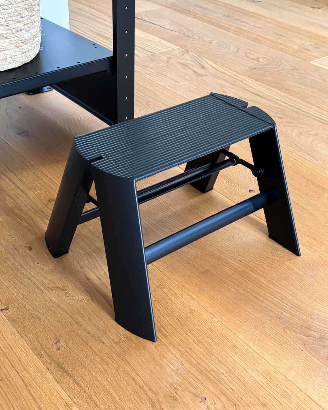 Schwarzer Tritthocker ALVA Mono auf Holzboden neben einem Regal