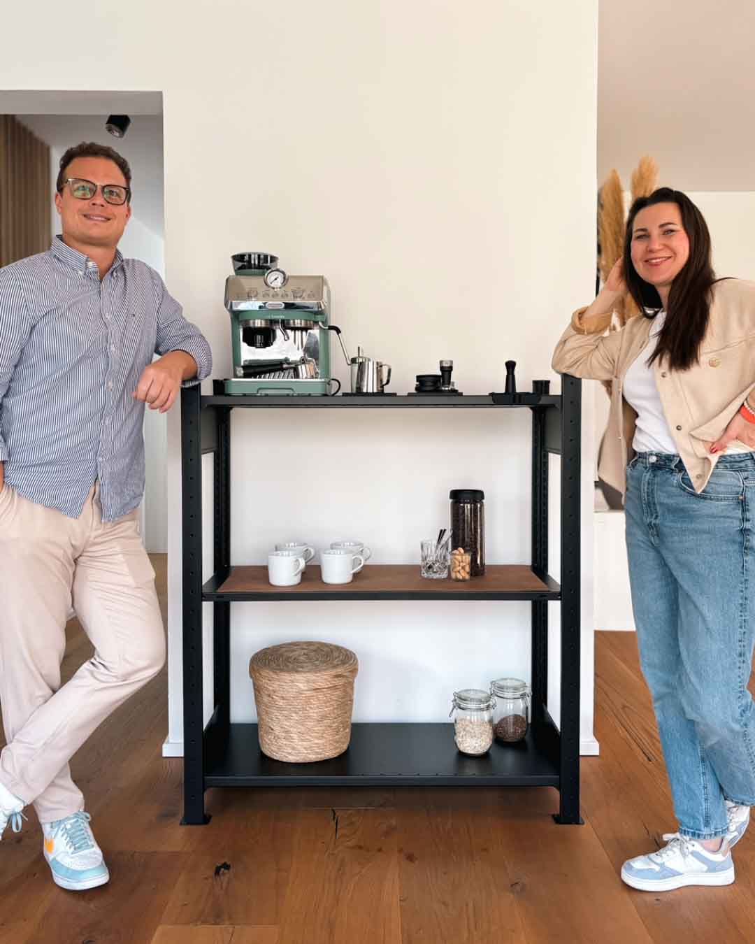 Zwei Personen neben dem schwarzen TILO Design Standregal aus Stahl mit Tassen und Kaffeemaschine