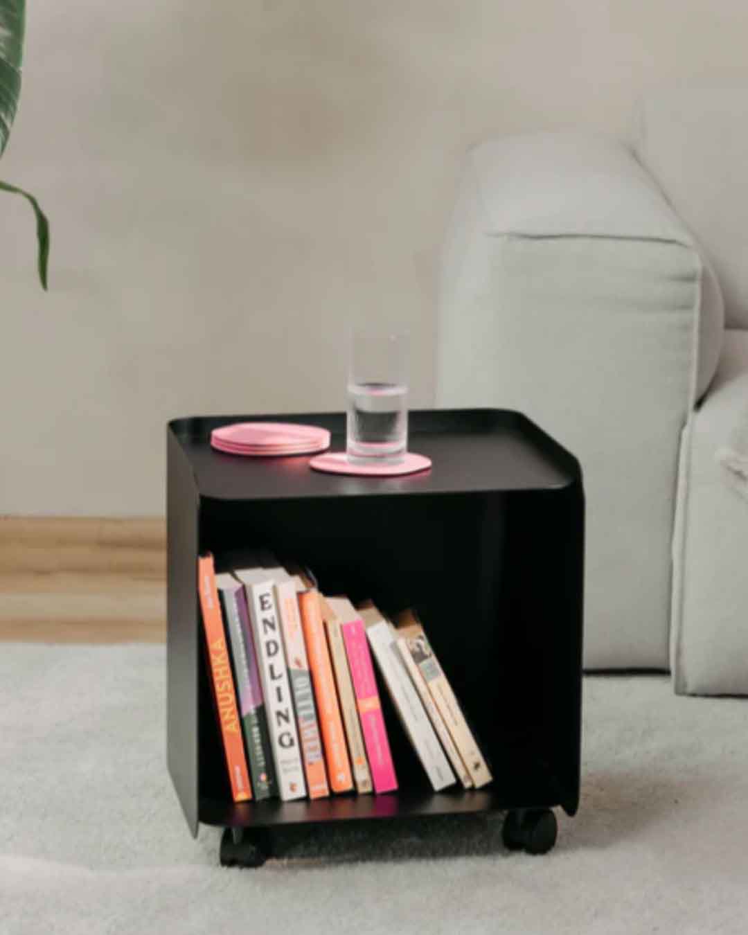 Schwarzer JUNO Rollcontainer in kleiner Ausführung neben einem Sofa mit Büchern und Glas