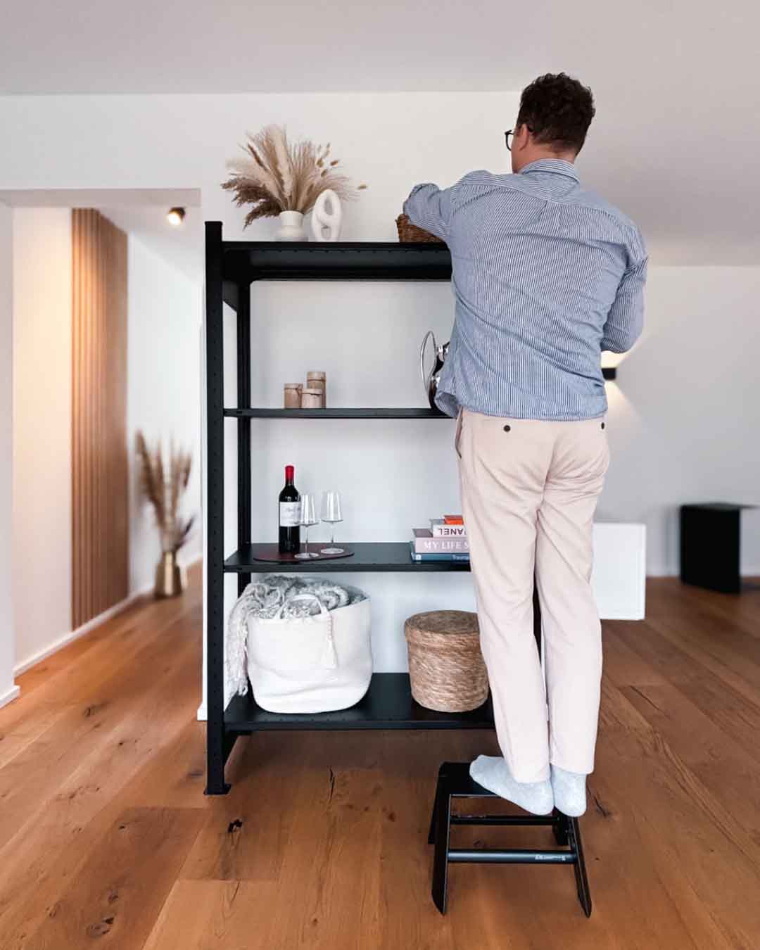 Schwarzer Tritthocker MICA mit Person in Anwendung vor einem schwarzen Regal