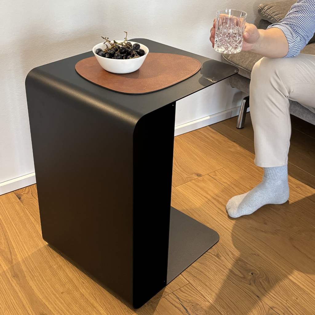 Braune Design-Unterlage aus recyceltem Leder auf einem schwarzen Beistelltisch mit Schale