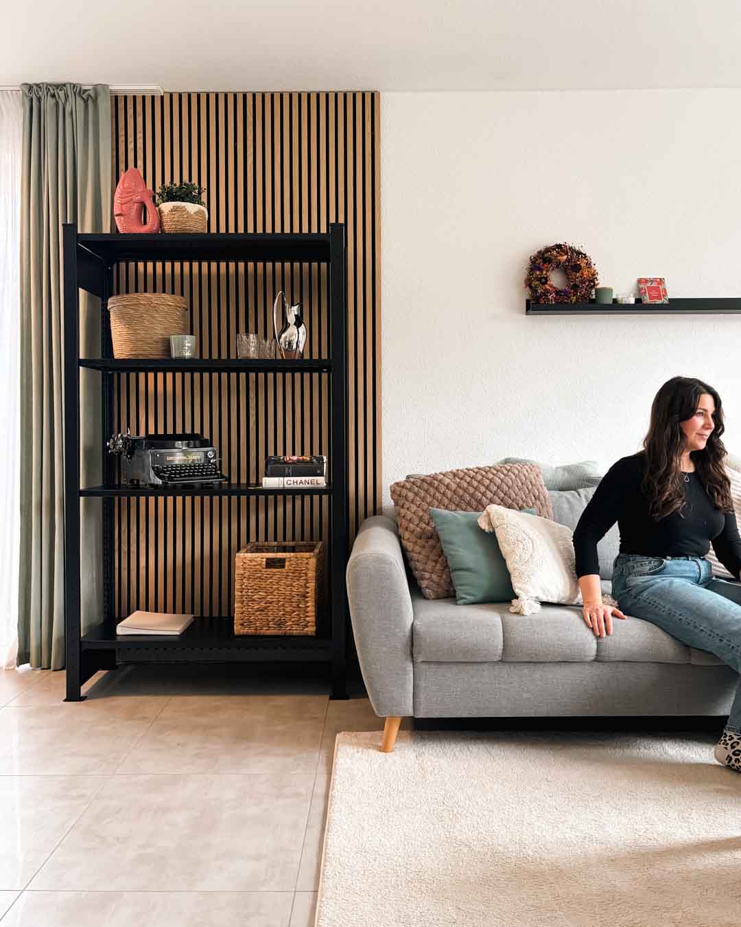 Schwarzes MICA Design Standregal aus Stahl mit 180 cm Höhe im Wohnraum neben einem Sofa mit Person